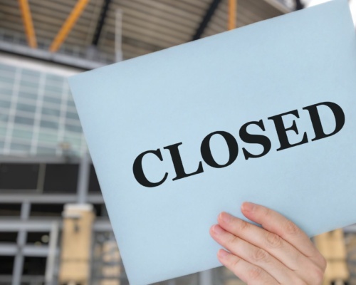 Closed-sign A hand holds a sign reading CLOSED in front of a modern building.