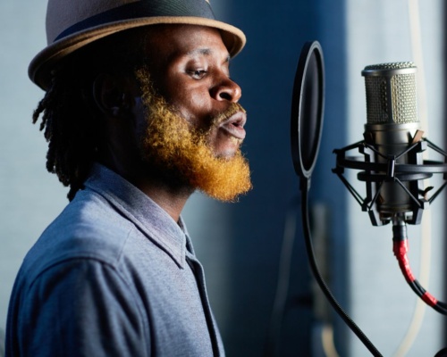 Connecting Through Authenticity Person wearing a hat and headphones singing into a microphone in a recording studio.