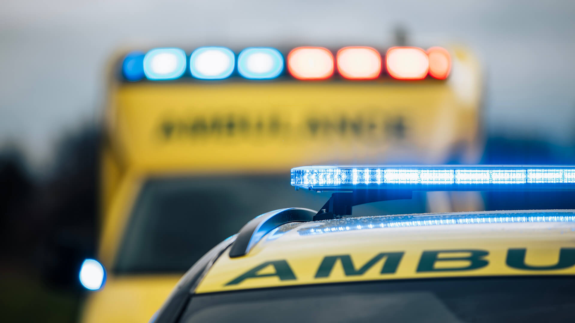 Close-up of an ambulance with blue emergency lights flashing, emphasising urgency akin to effective business communication; another emergency vehicle and its red and blue lights appear blurred in the background.