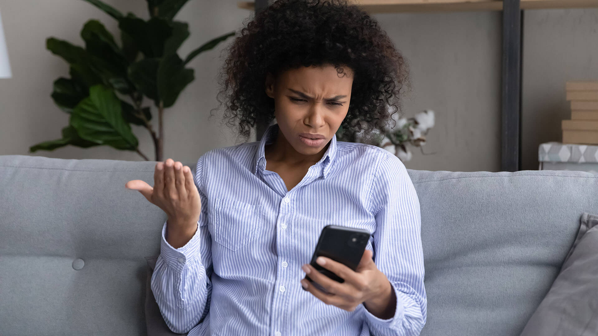 blog-annoyed-on-phone A person sitting on a settee looks at their mobile with a confused and frustrated expression, holding one hand up in disbelief.