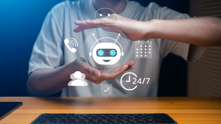 A person cups their hands around a floating robot icon, encircled by digital communication symbols, representing artificial intelligence in answering service versus virtual receptionist solutions.
