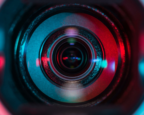 Close-up of a camera lens reflecting blue and red light, ideal for producing instructional explainer videos.