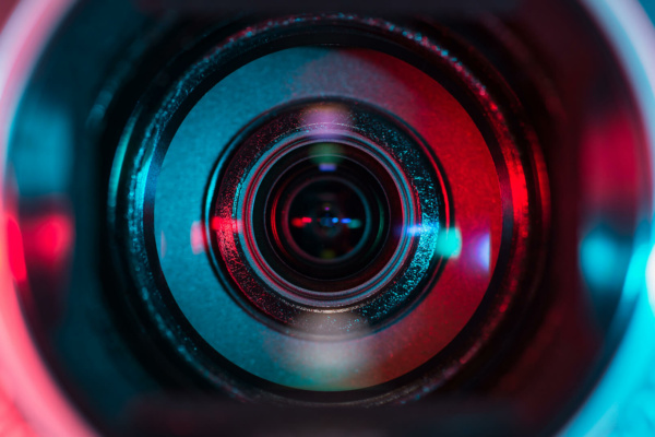 Close-up of a camera lens reflecting blue and red light, ideal for producing instructional explainer videos.