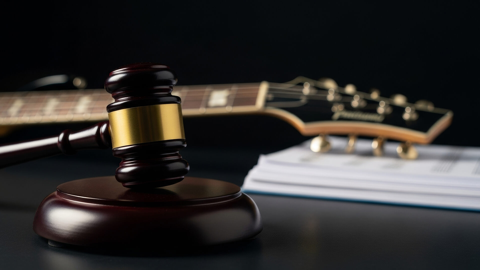 A judge’s gavel rests before a guitar and a pile of documents on a dark surface, representing legal issues concerning music or intellectual property.