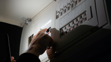 A person’s hand switches a circuit breaker on an electrical distribution board.