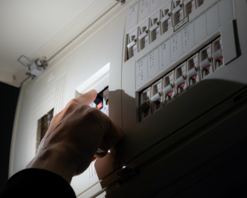 A person’s hand switches a circuit breaker on an electrical distribution board.