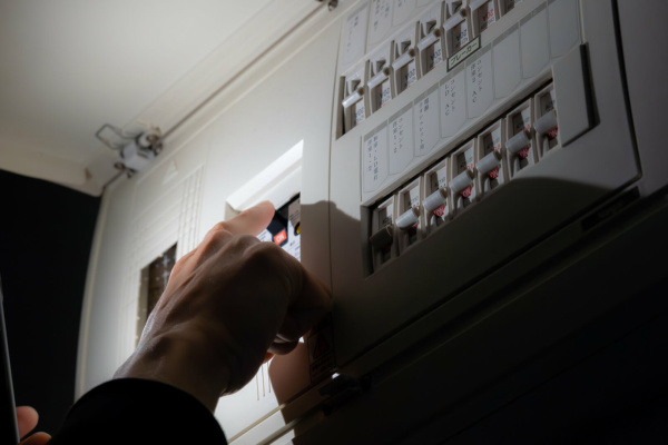 A person’s hand switches a circuit breaker on an electrical distribution board.