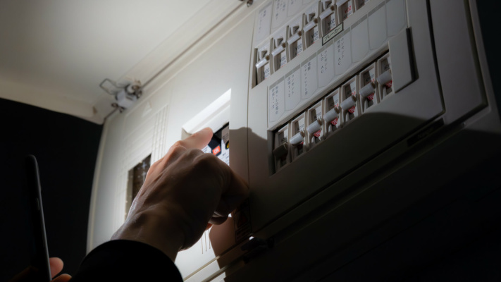 blog-power-cut A person’s hand switches a circuit breaker on an electrical distribution board.