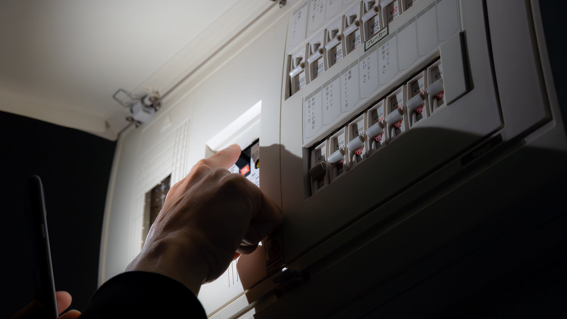 A person’s hand switches a circuit breaker on an electrical distribution board.