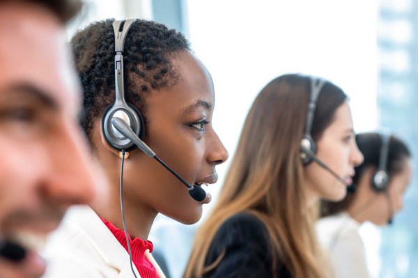 Four customer service representatives wearing headsets are seated in a row, concentrating on temporary call handling in a modern office environment.