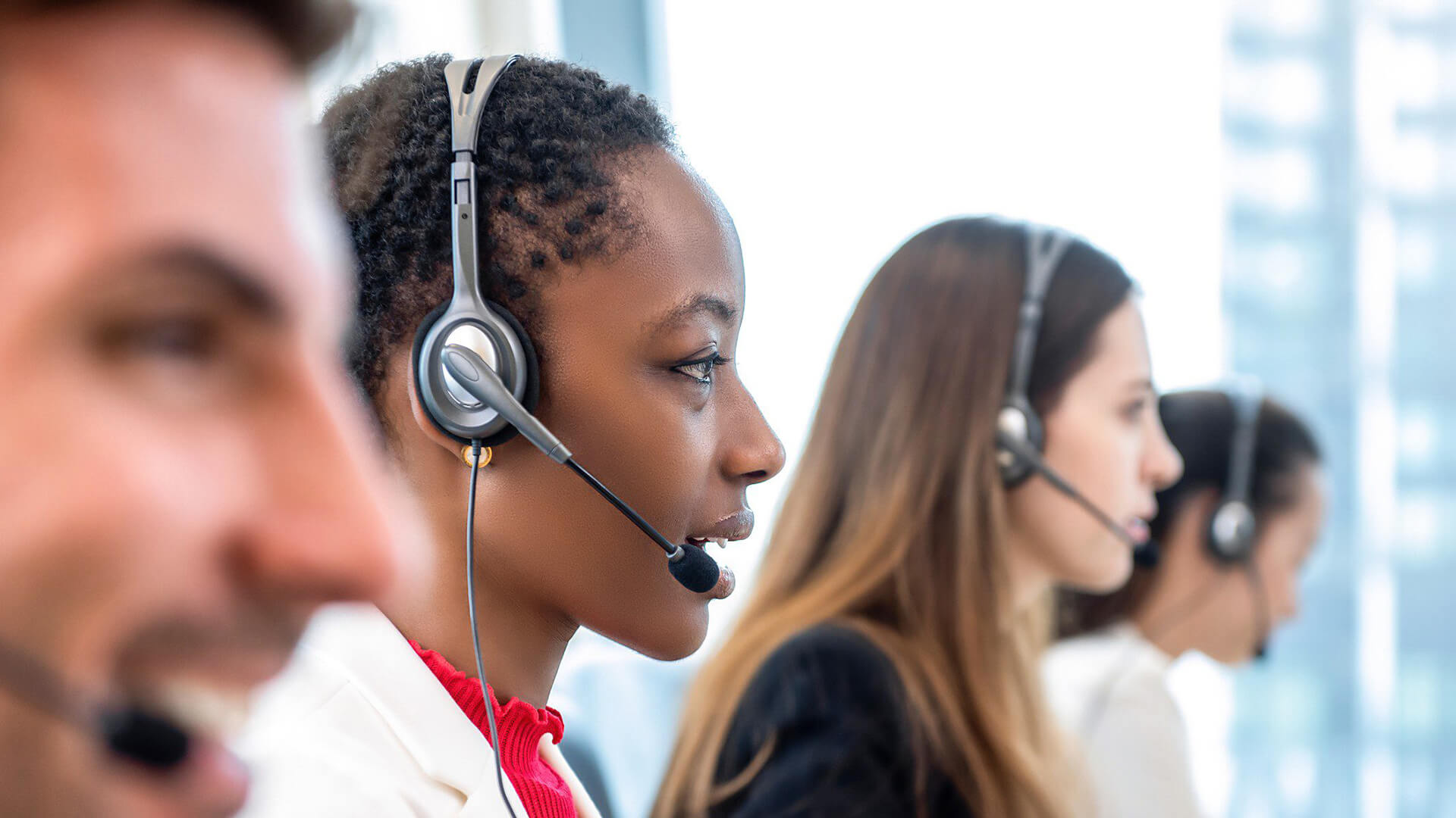 Four customer service representatives wearing headsets are seated in a row, concentrating on temporary call handling in a modern office environment.