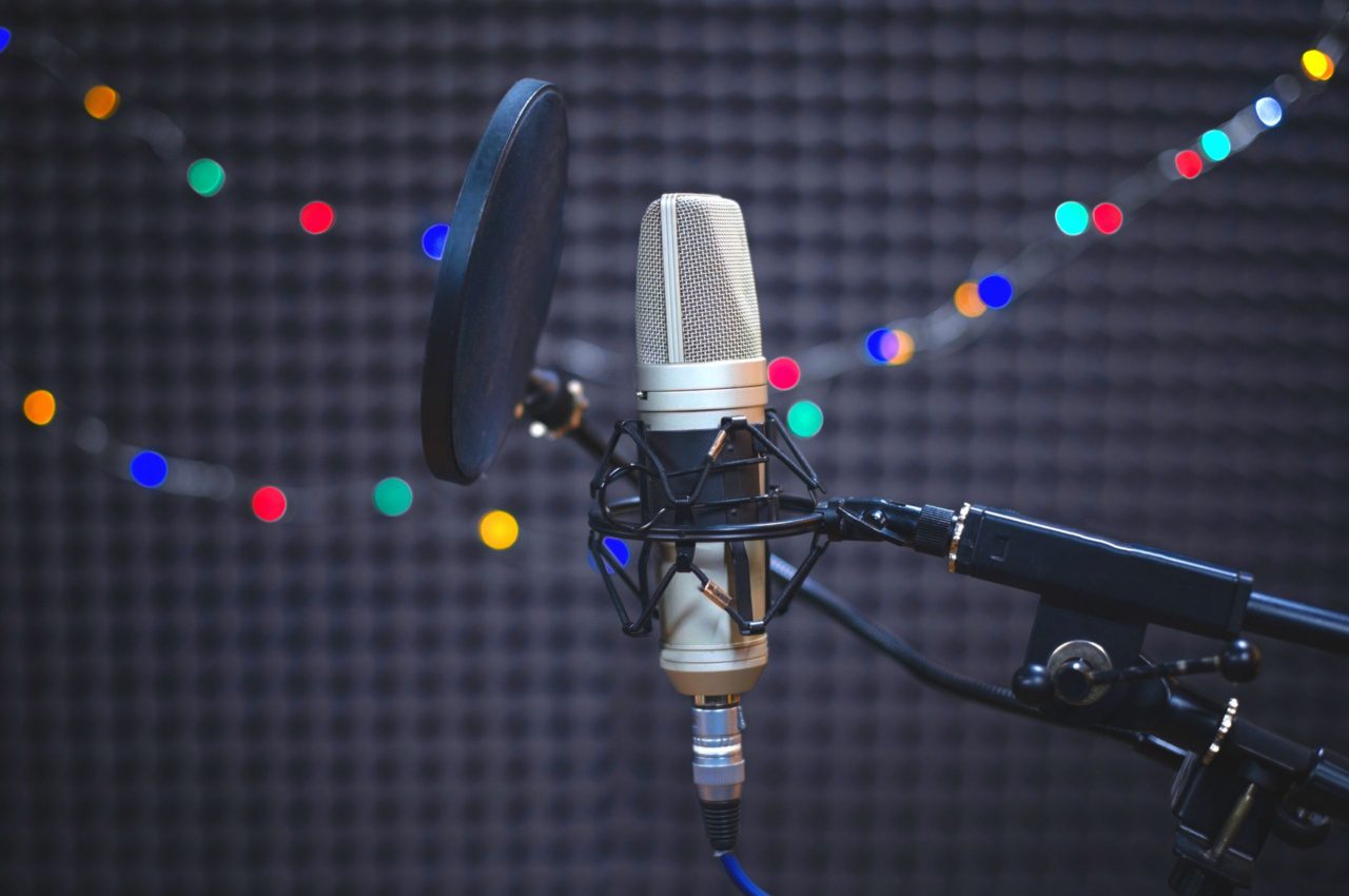 A microphone with a pop filter is set up in a sound booth, ready for an overseas voice-over session. LED lights are blurred in the background, creating an ambient glow.