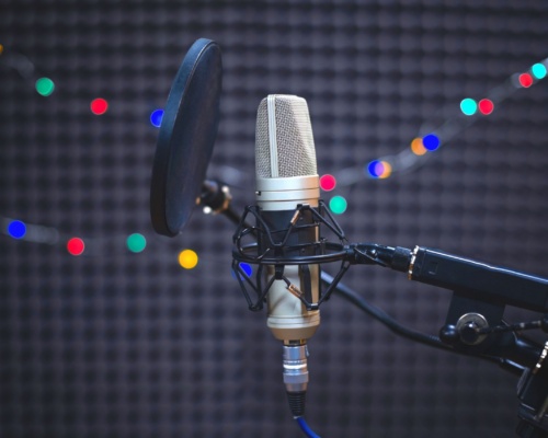 microphone A microphone with a pop filter is set up in a sound booth, ready for an overseas voice-over session. LED lights are blurred in the background, creating an ambient glow.