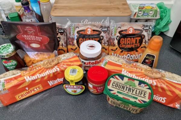 An assortment from Onhold Studio featuring a variety of crumpets, spreads, cheese, butter, and sauces graces the kitchen counter. The selection includes Warburtons crumpets, Nutella, Marmite, Lotus Biscoff, and Country Life butter.