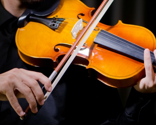 person playing a violin A person in black holds and plays a violin with a bow.
