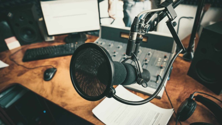 professional-voiceover-studio A professional voiceover studio showcasing a microphone in a recording setup, complete with a mixing console, computer screen, keyboard, and headphones on a polished wooden desk.