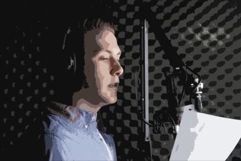 A professional voiceover artist, wearing headphones, speaks smoothly into the microphone inside a soundproof booth, holding a script in hand.